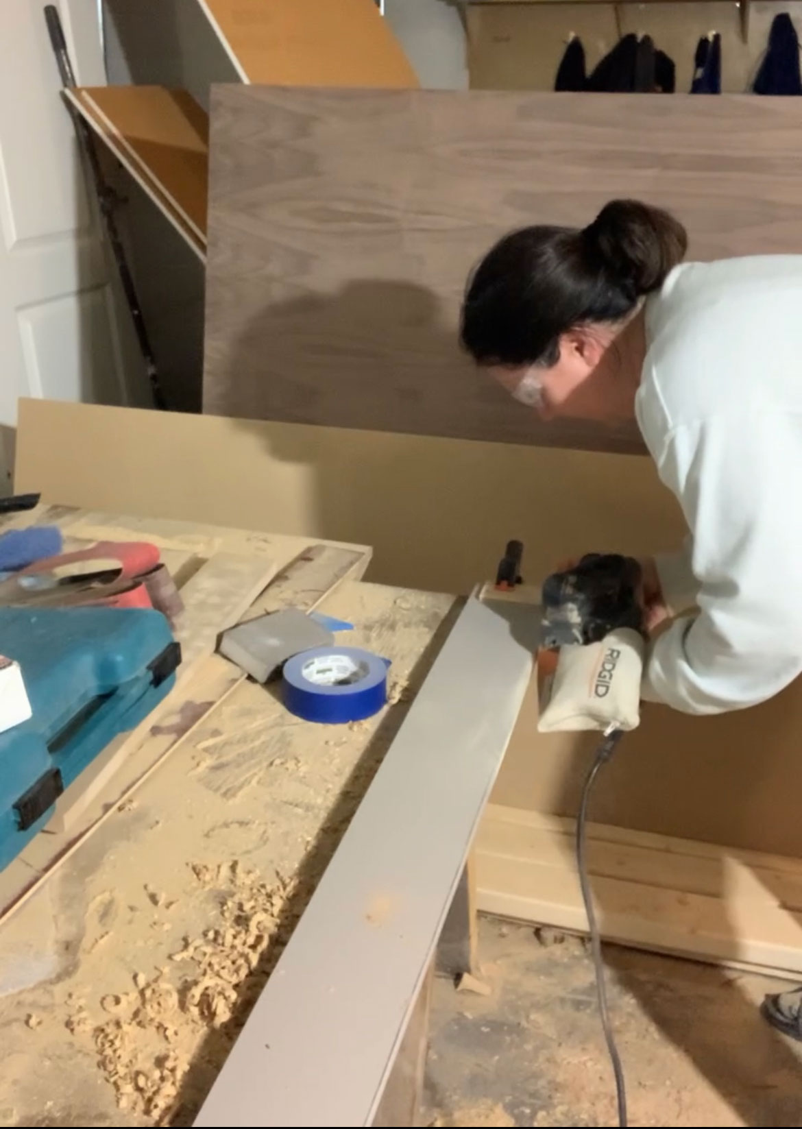 a cabinet toe kick clamped to a bench and woman sanding the edge with a belt sander