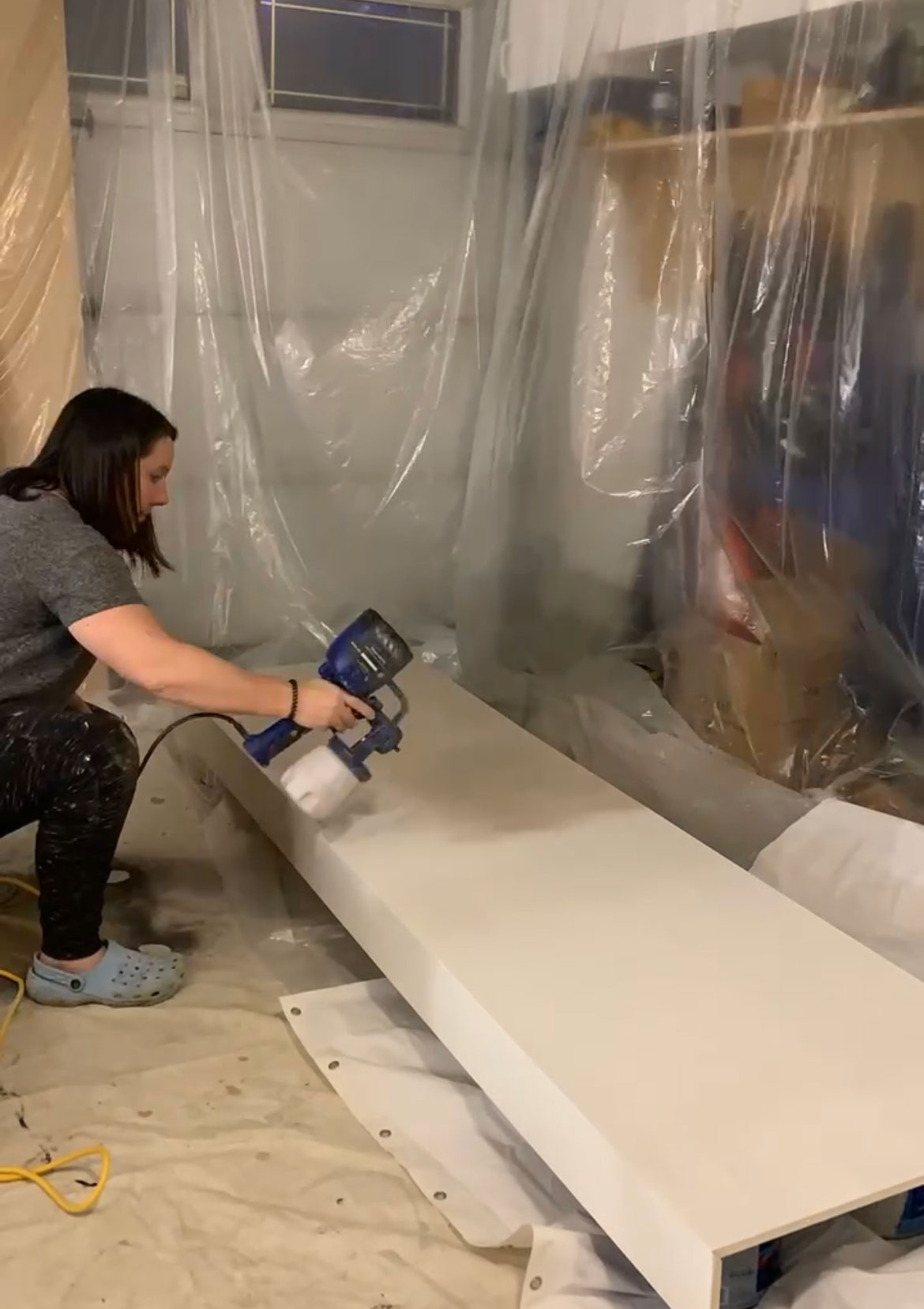 woman using a hand held sprayer to spray a large panel on the ground with brown paint
