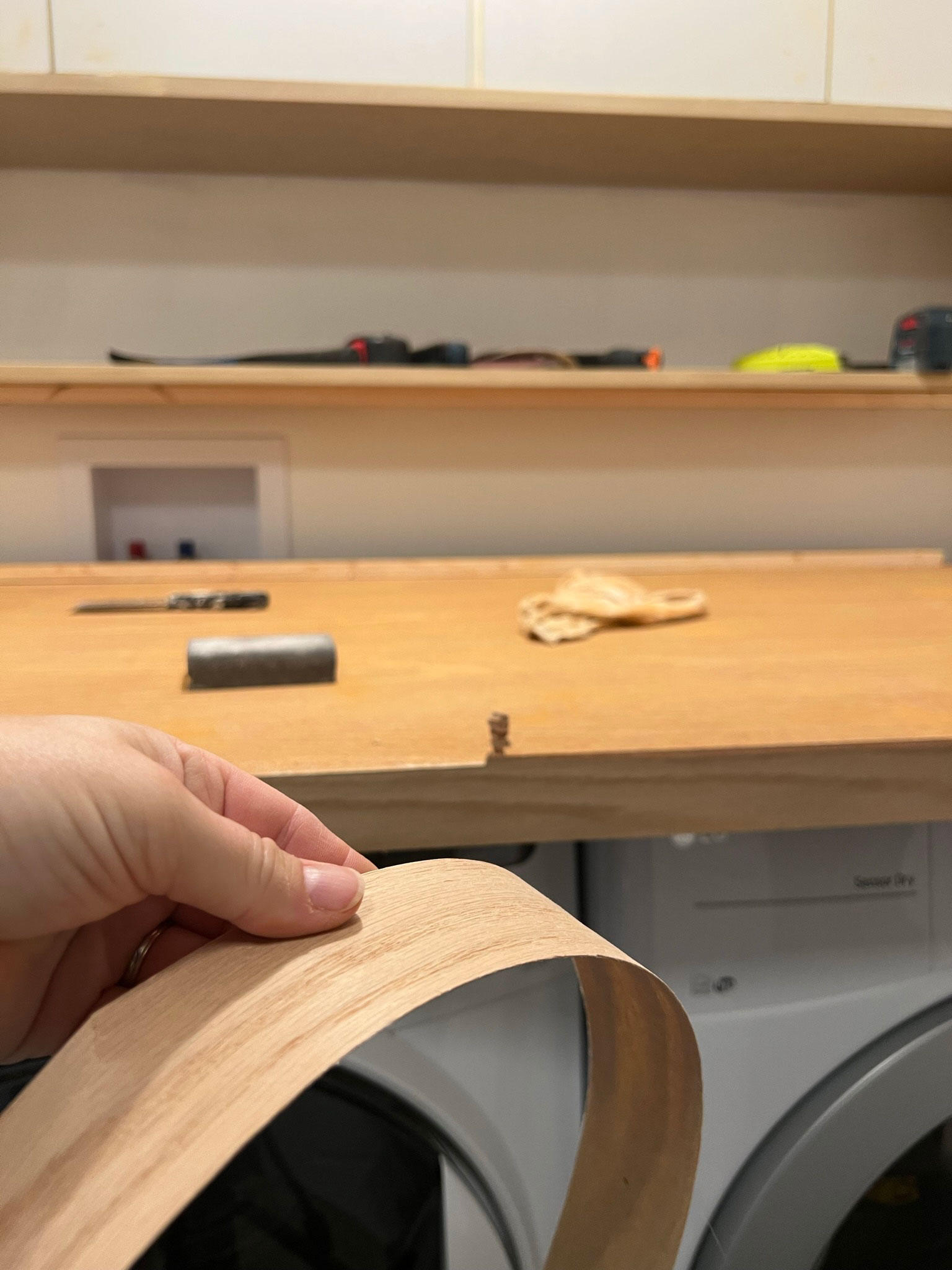 holding a piece of veneer to show how thin it is, and veneered door in the background with the edges of the veneer in the process of being removed for the DIY laundry room countertop