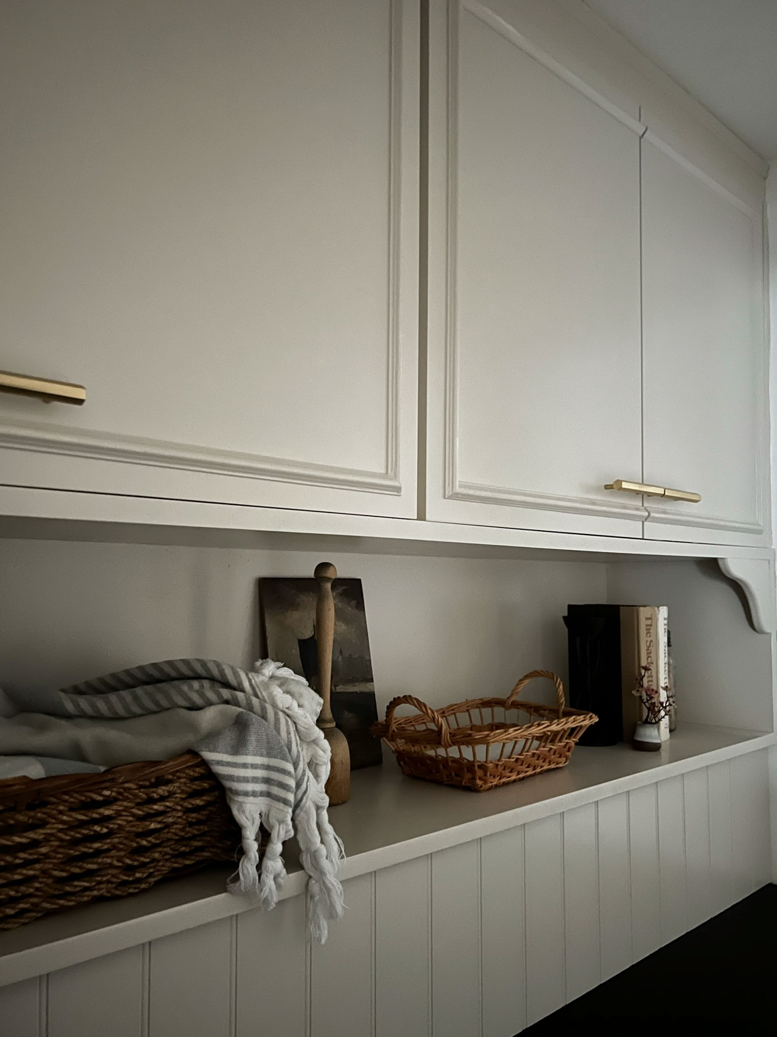 beige cabinets with trim attached and a shelf below with styling accessories