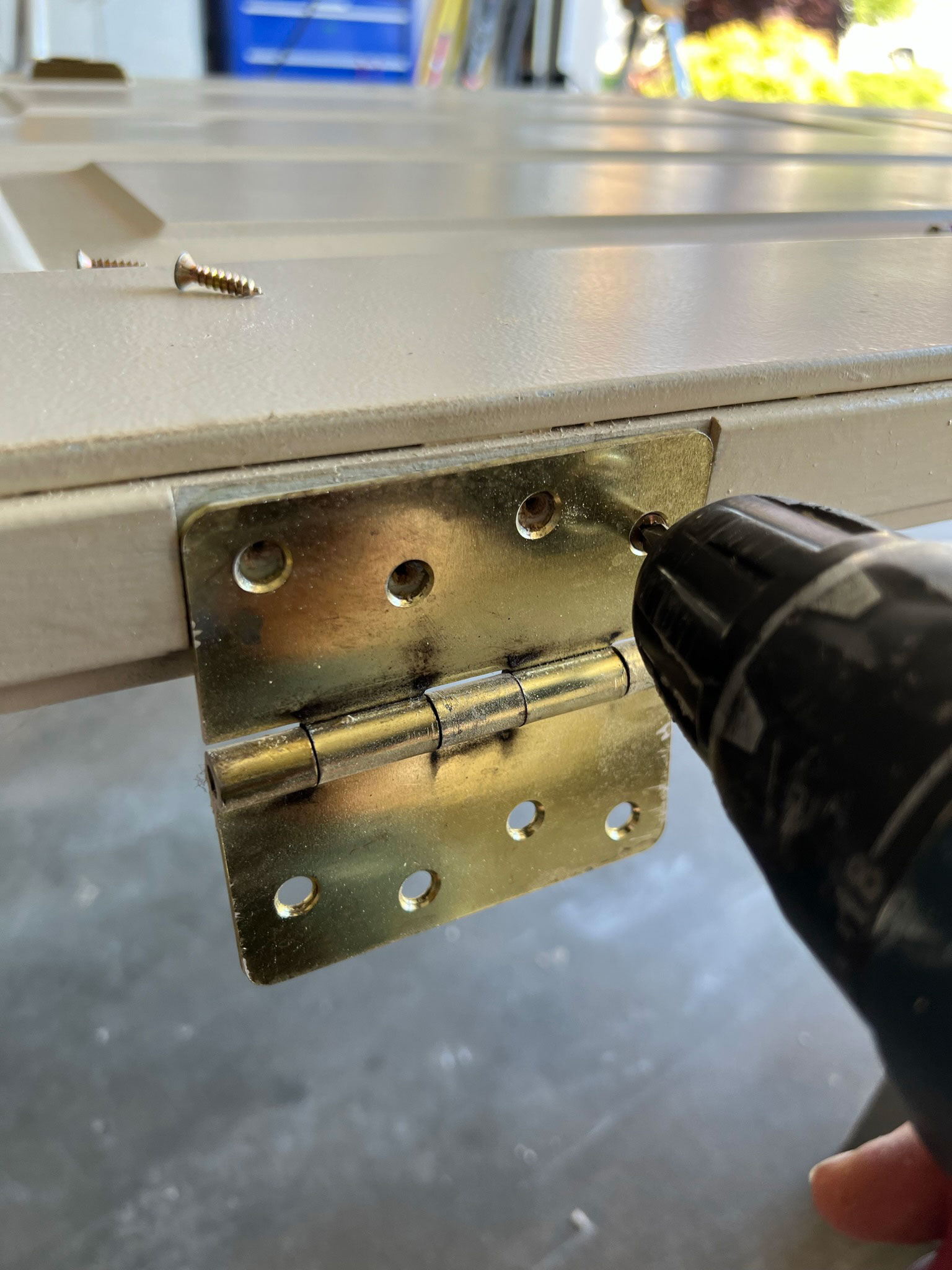 using a drill to unscrew brass door hinges from a door
