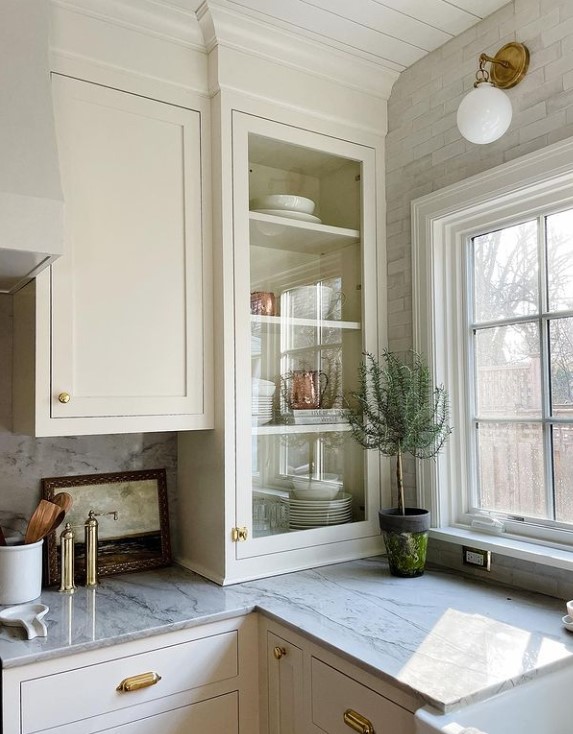 off white kitchen with glass corner countertop cabinet adjacent to a window