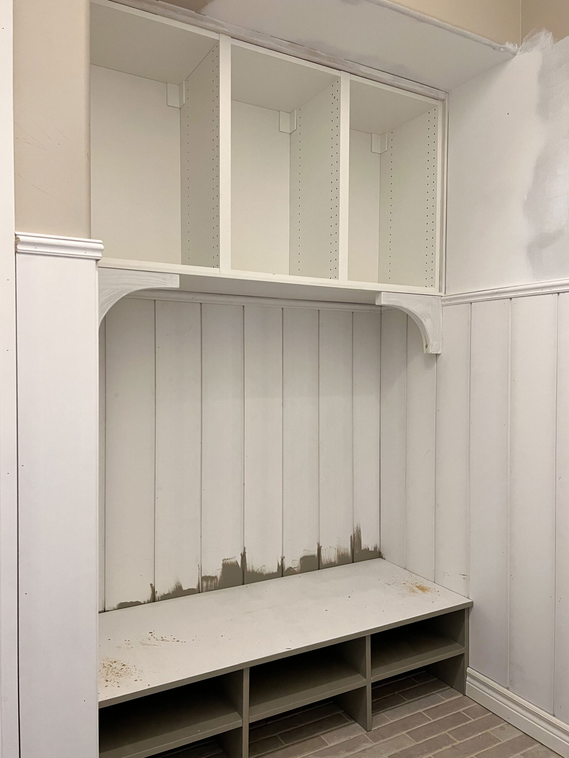 primed mudroom bench with corbels in the corner and shiplap walls, open cabinets above and below