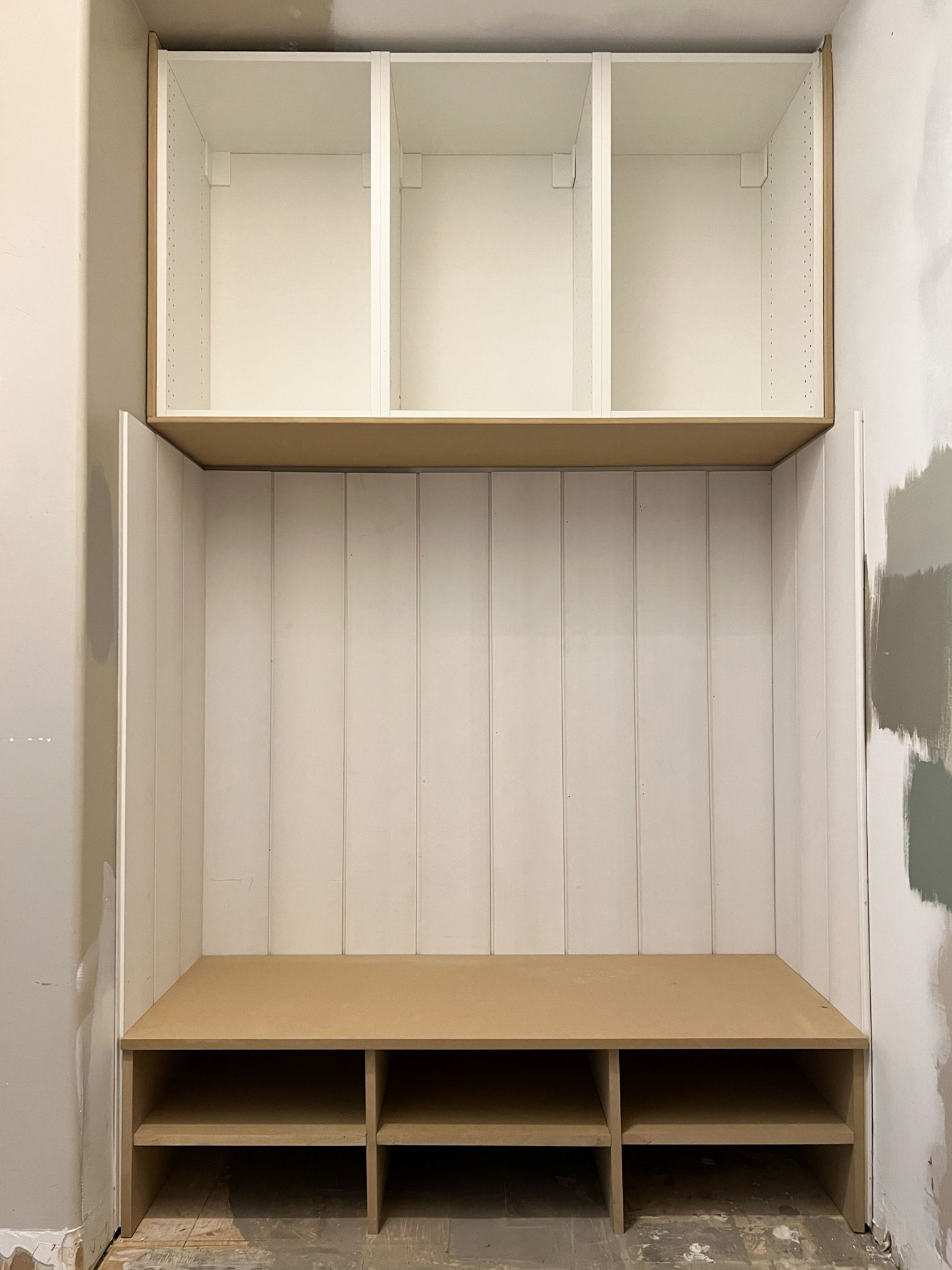 unfinished mudroom bench with cabinets above and shiplap walls