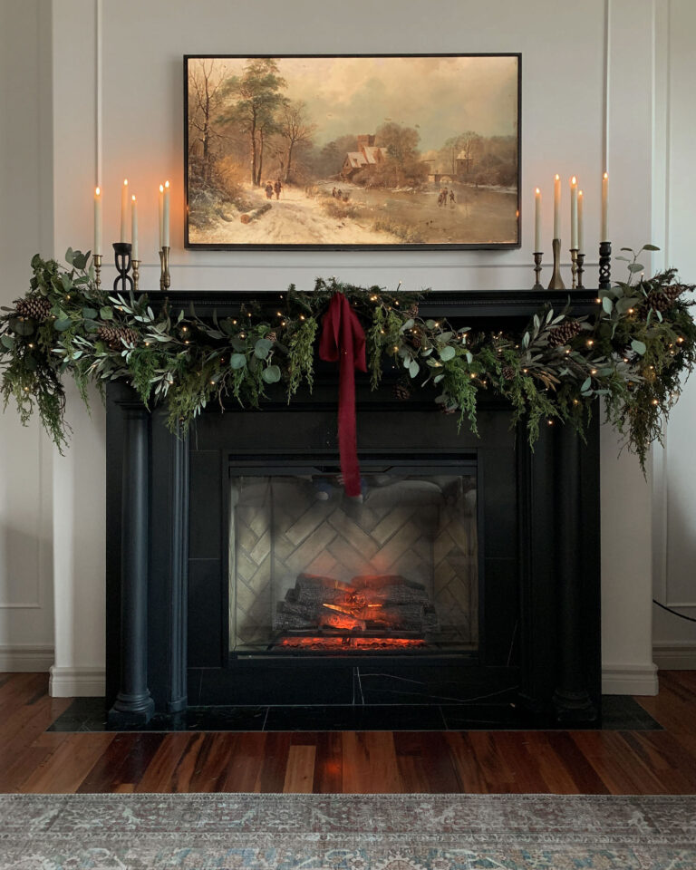black fireplace with garland, fire going, brass candles and art above