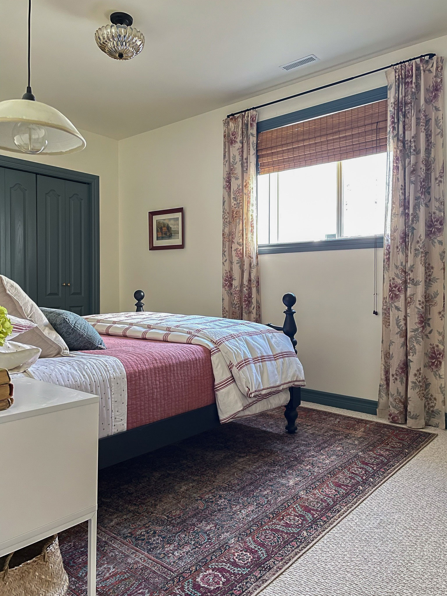 bedroom with blue trim and floral curtains, red rug, black bed with pink striped duvet