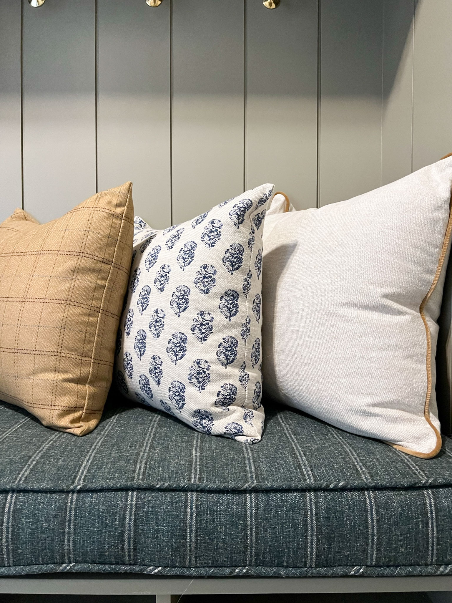 brown plaid pillow, blue block print pillow and white with brown piping pillow on a blue striped bench cushion 