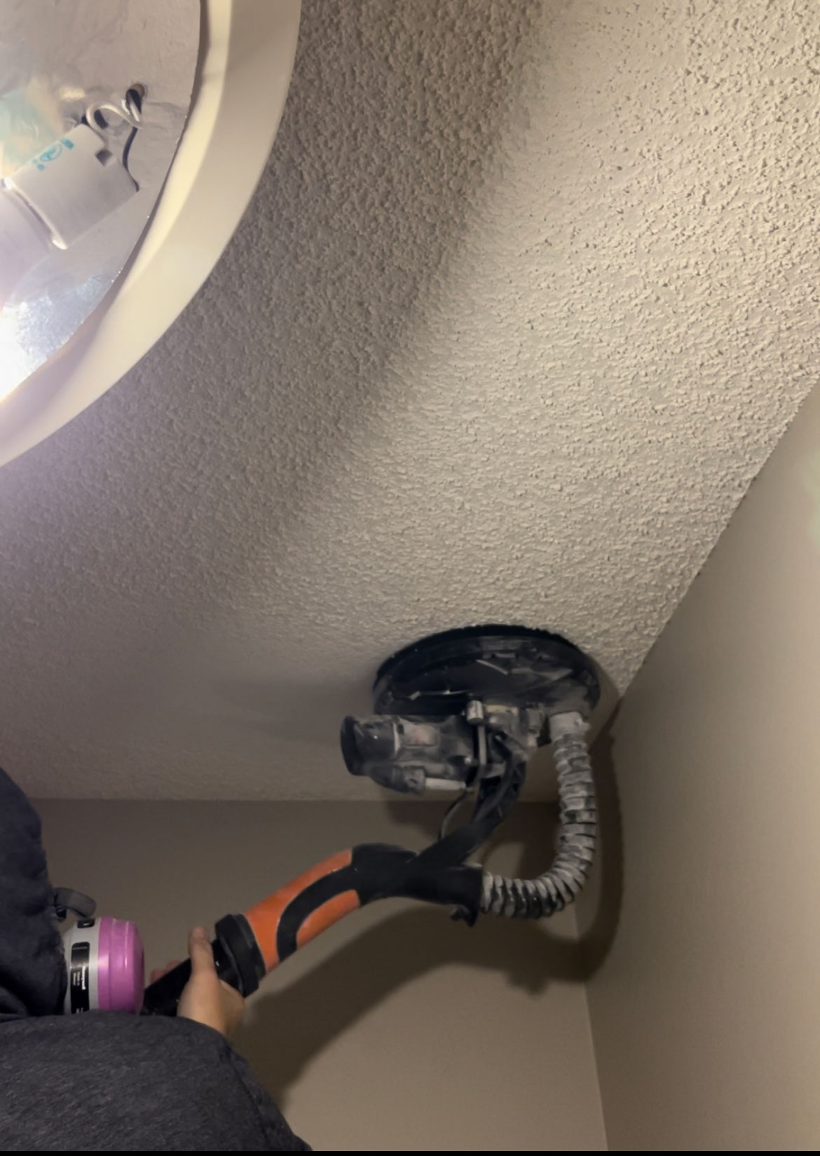 woman in a face mask using a drywall sander to remove popcorn ceiling