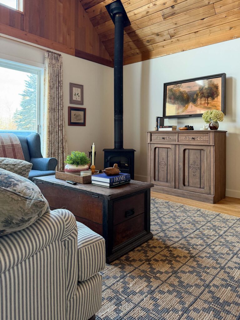 cozy living room with striped roll arm sofa, antique furniture, blue chair and lots of pillows, and a blue chair.