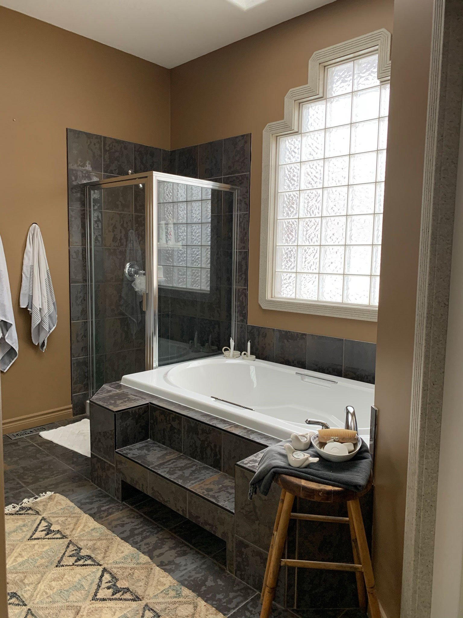 ensuite bathroom with large grey tiled tub, grey tile, glass block window