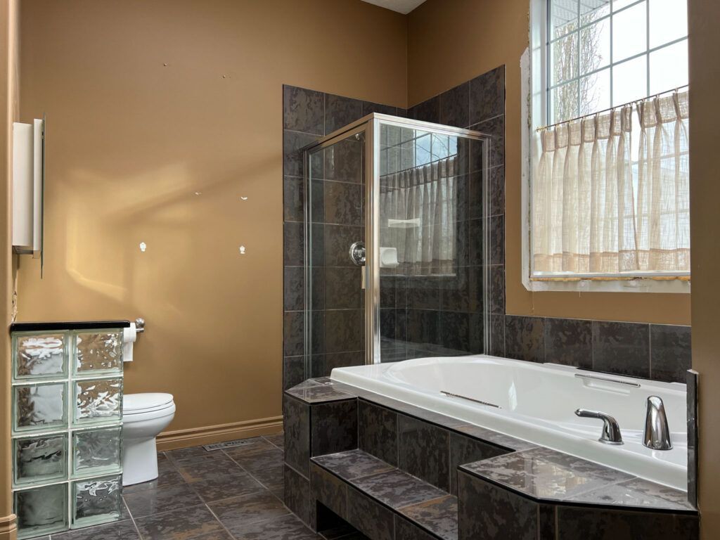 90's bathroom with large grey tiled tub, corner shower, glass block partition, brown walls