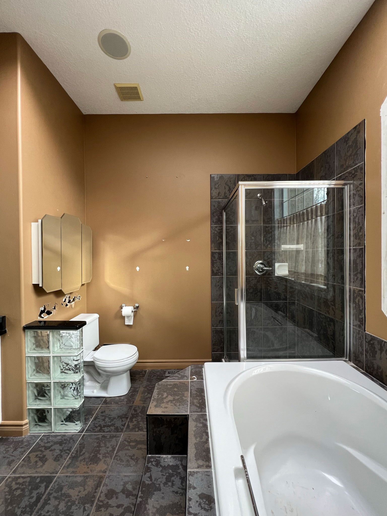 90's bathroom with large grey tiled tub, corner shower, glass block partition, brown walls