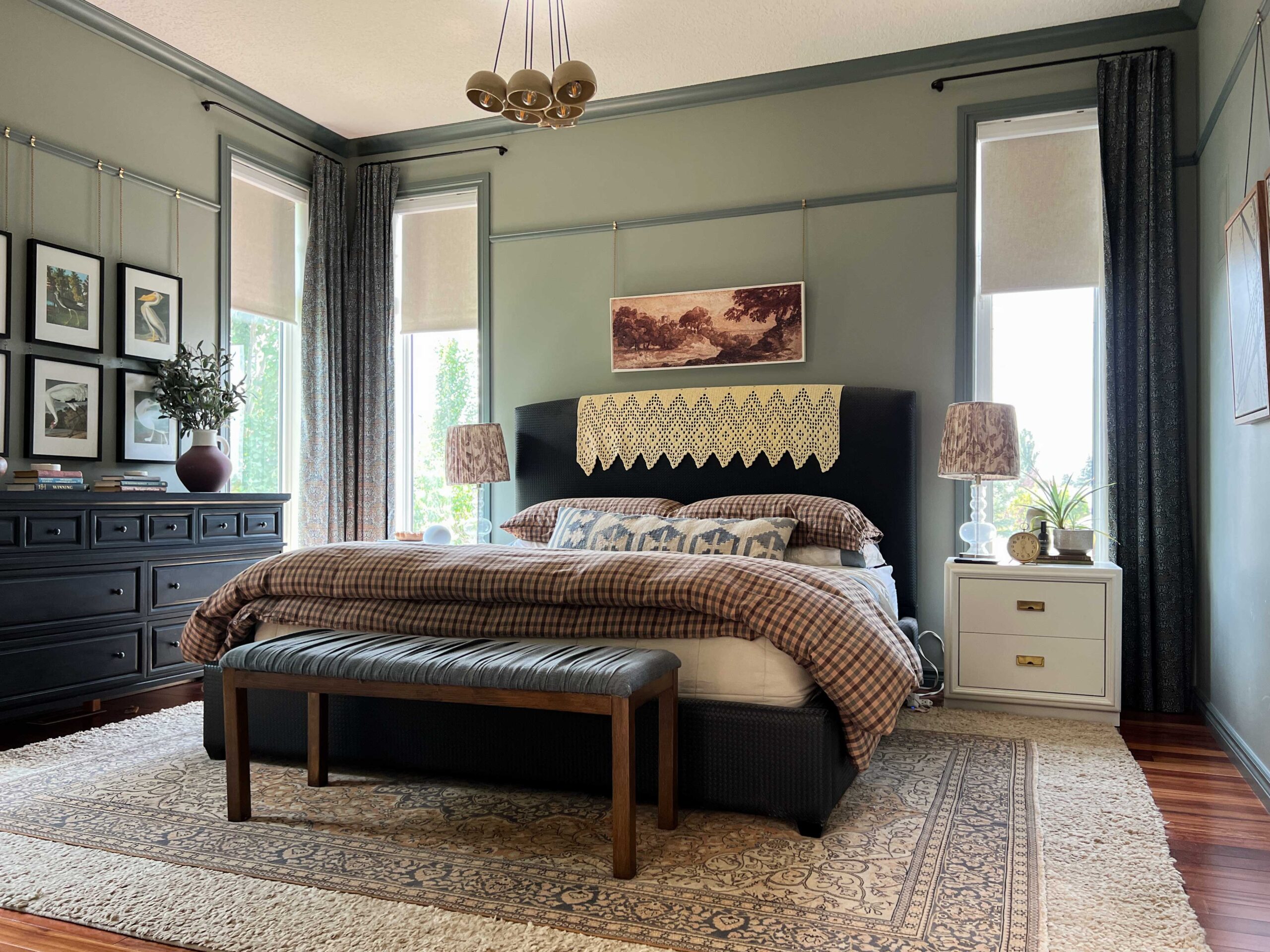 Bedroom with green walls and dark green trim, black bed, blinds half closed, patterned curtains