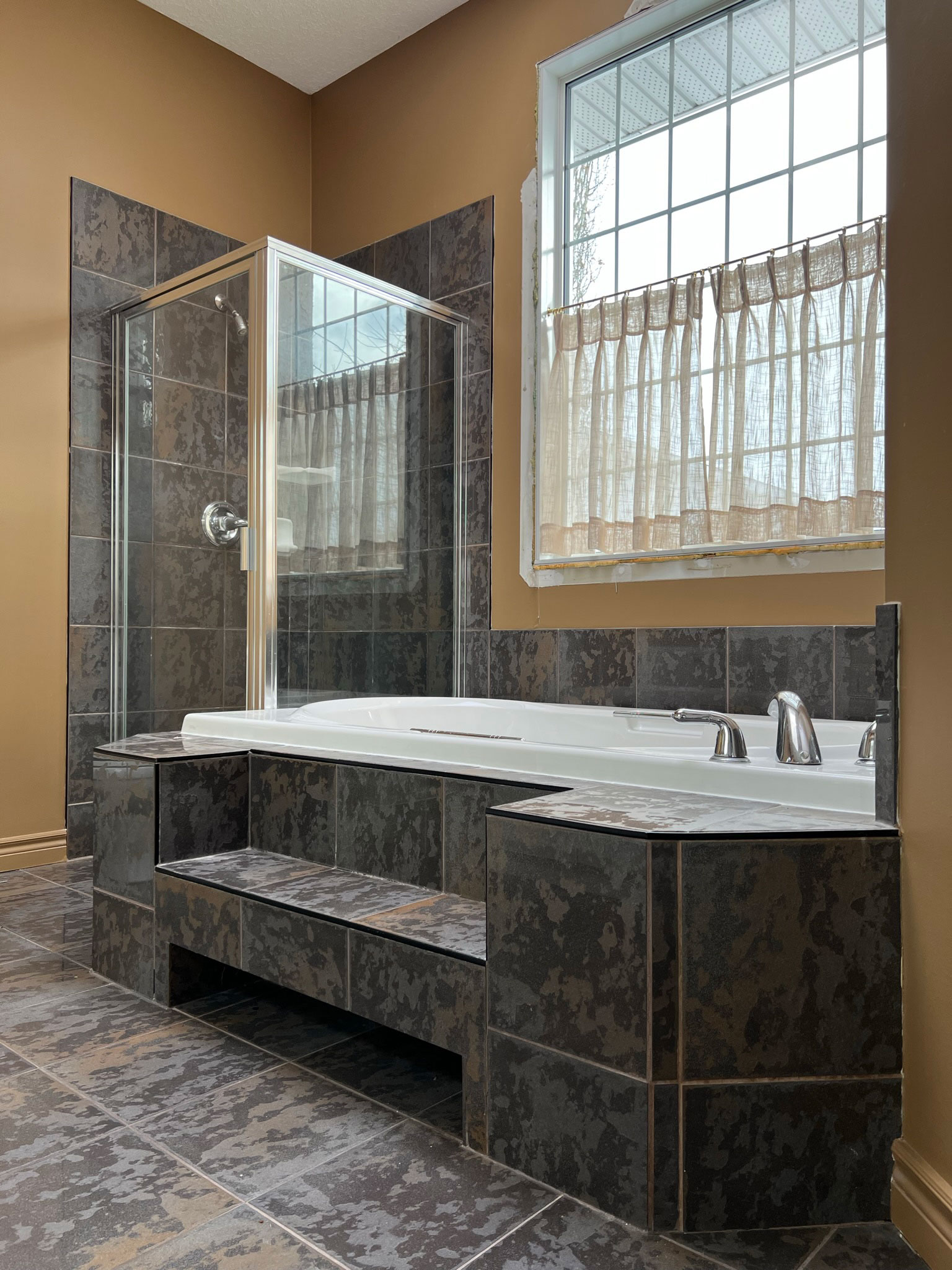 90's bathroom with large grey tiled tub, corner shower, glass block partition, brown walls