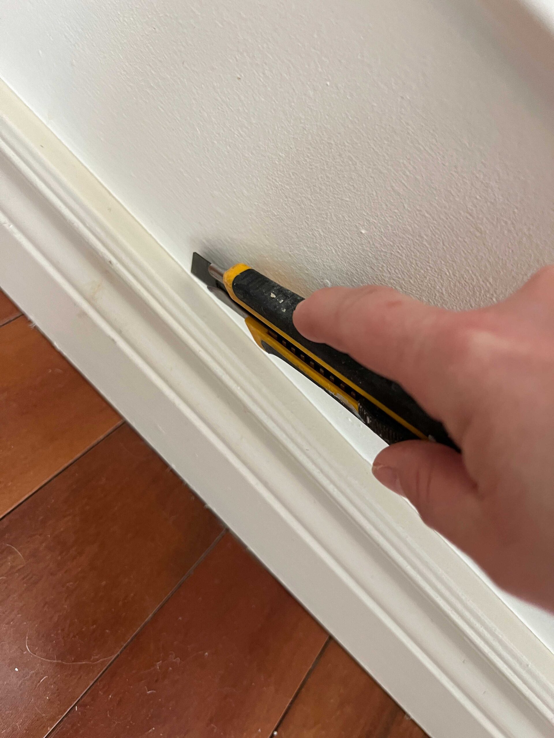 Using utility knife to cut along top of baseboard prior to removing