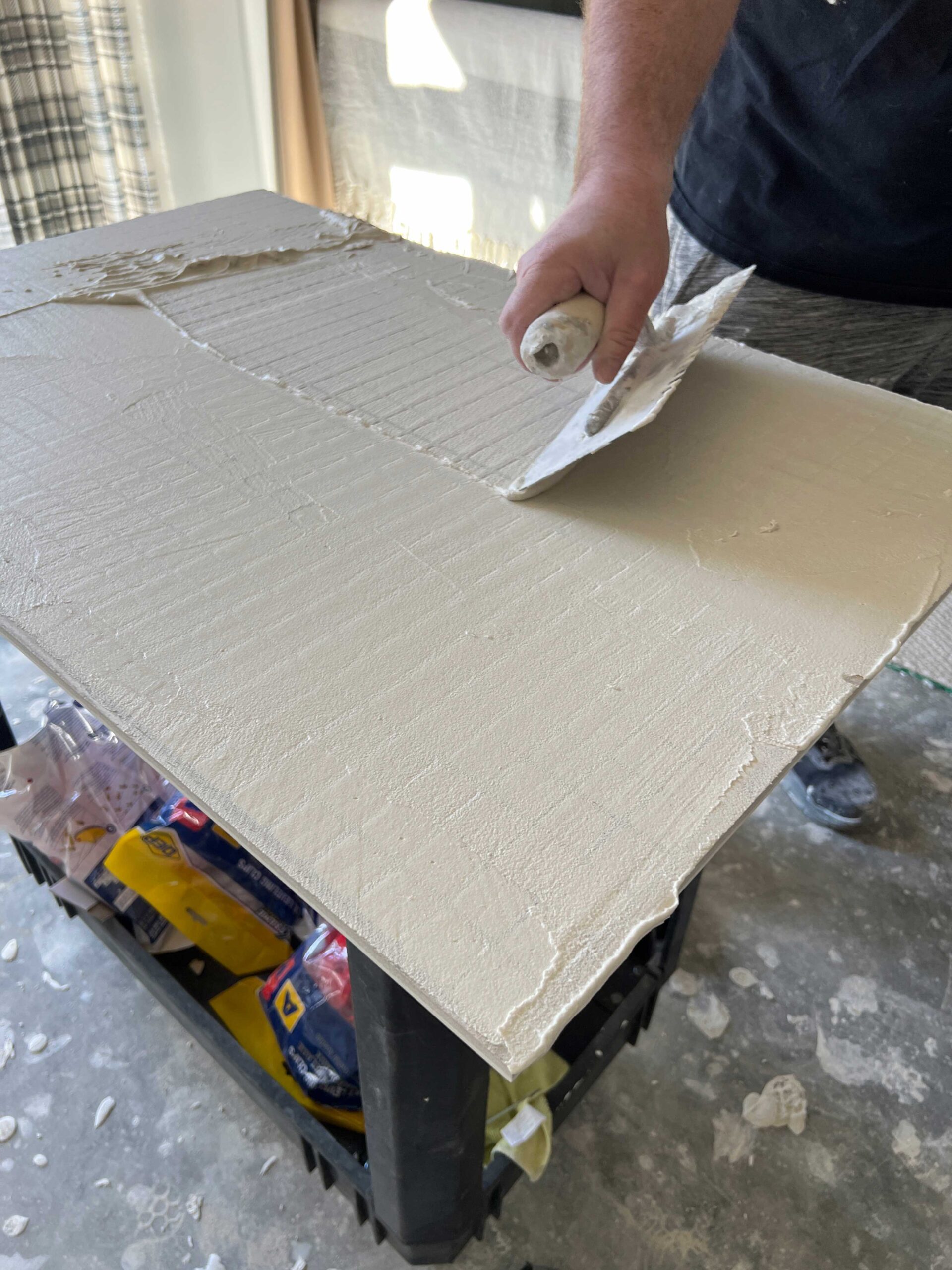 using flat side of trowel to back butter tile