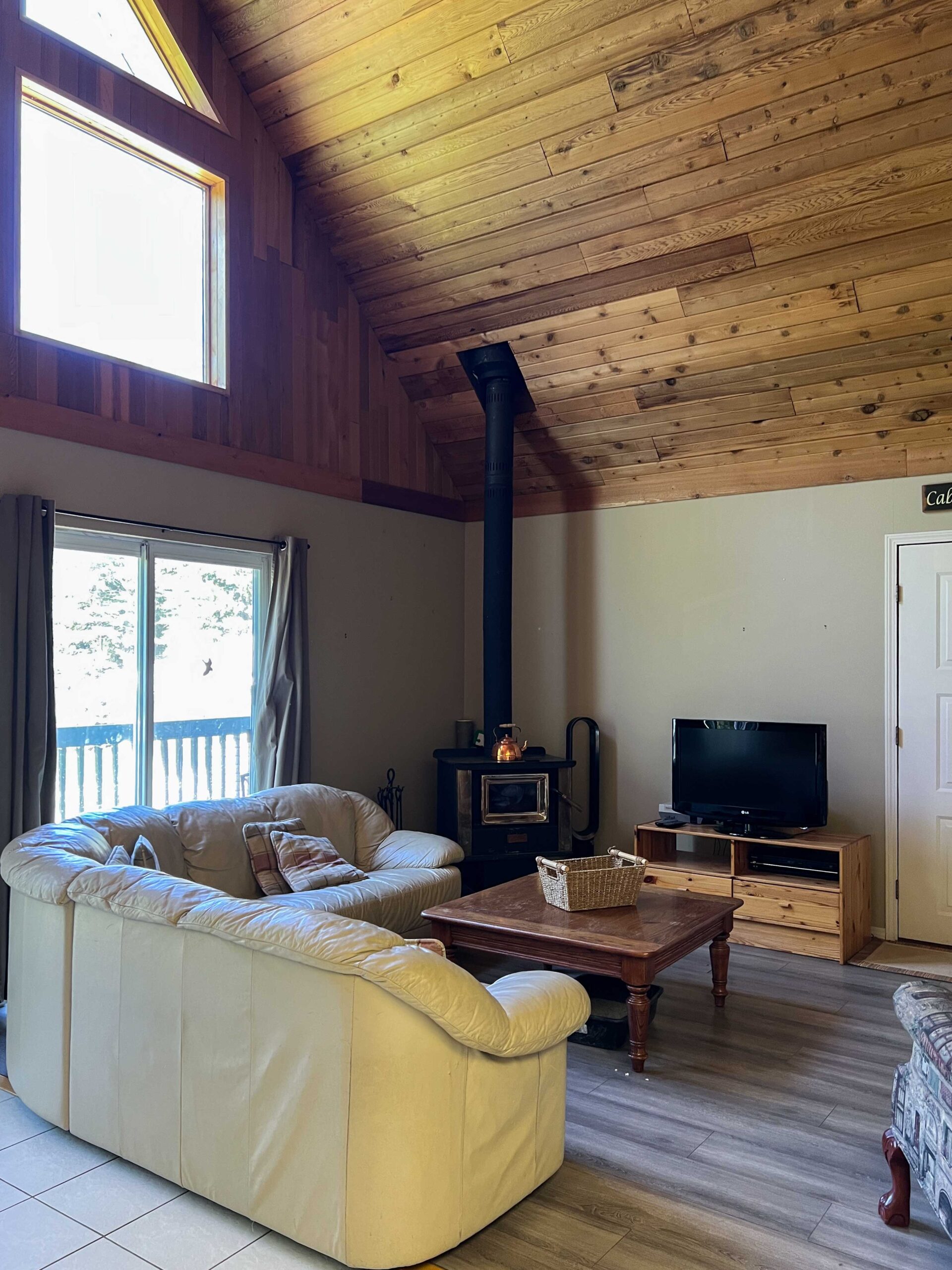 cabin living room with corner wood fired stove, leather 80's sectional and grey floor