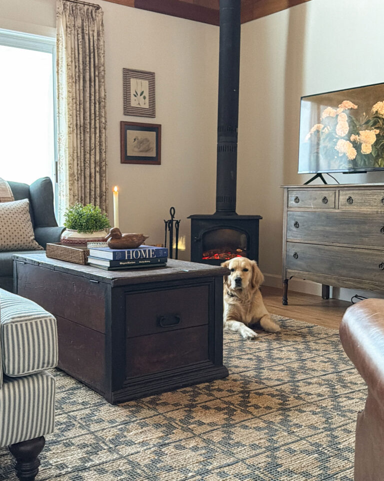 cozy living room with striped roll arm sofa, antique furniture, blue chair and lots of pillows, and a blue chair, with a wood stove and dog