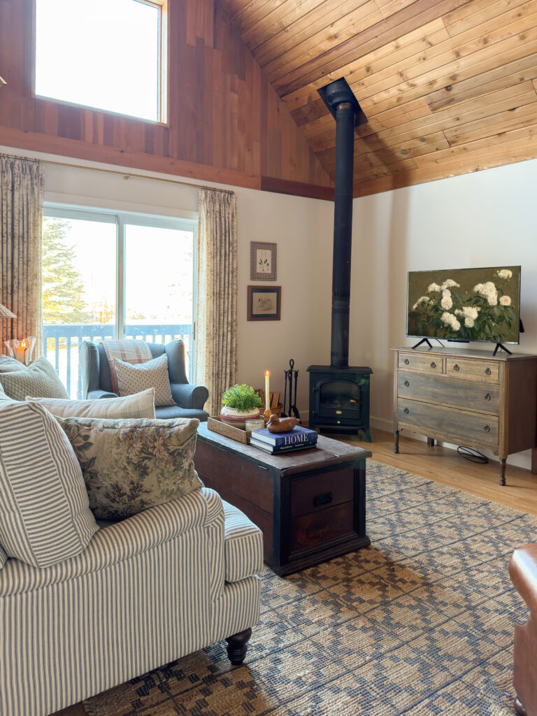 cozy living room with striped roll arm sofa, antique furniture, blue chair and lots of pillows, and a blue chair.