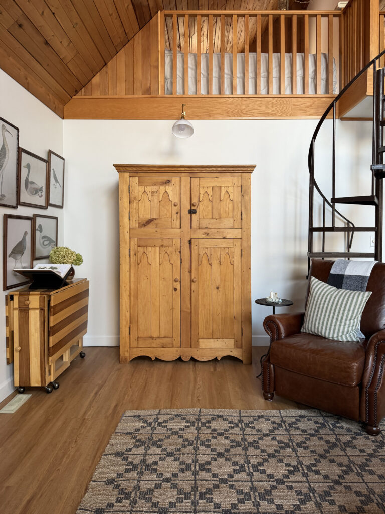 Pine antique armoire and a leather chair in front of a spiral staircase