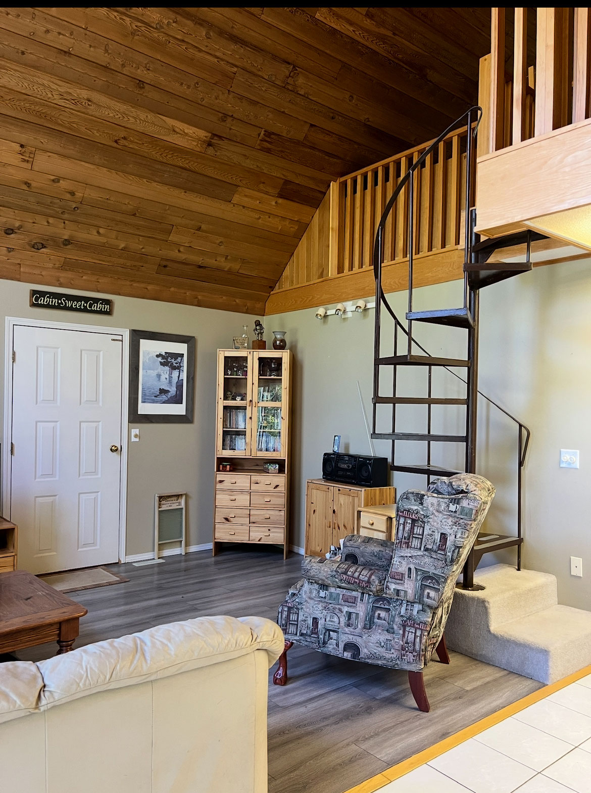 before photo of a dated living room with wood ceiling and grey laminate floor and a spiral staircase