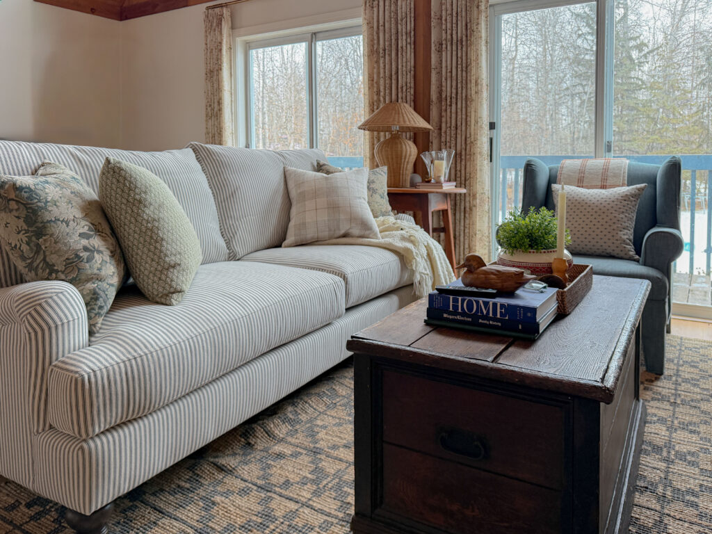 cozy living room with striped roll arm sofa, antique furniture, blue chair and lots of pillows, and a blue chair, with a wood stove 