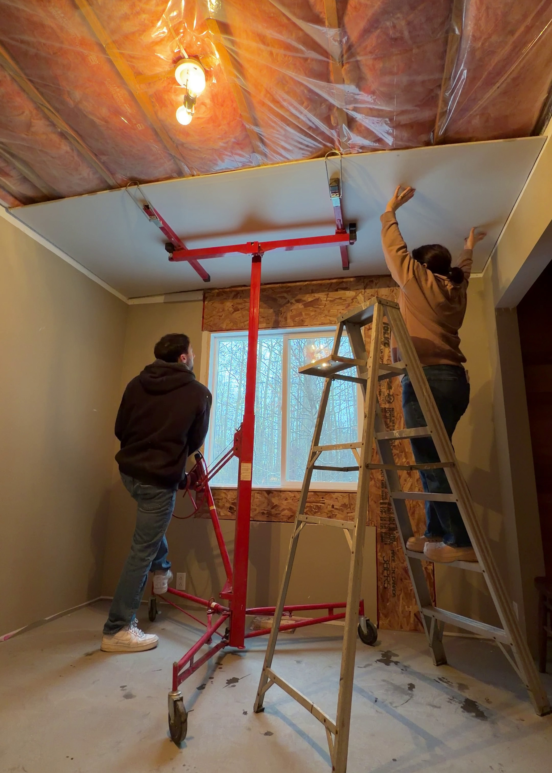 two people using a lift and ladder to install drywall on a ceiling