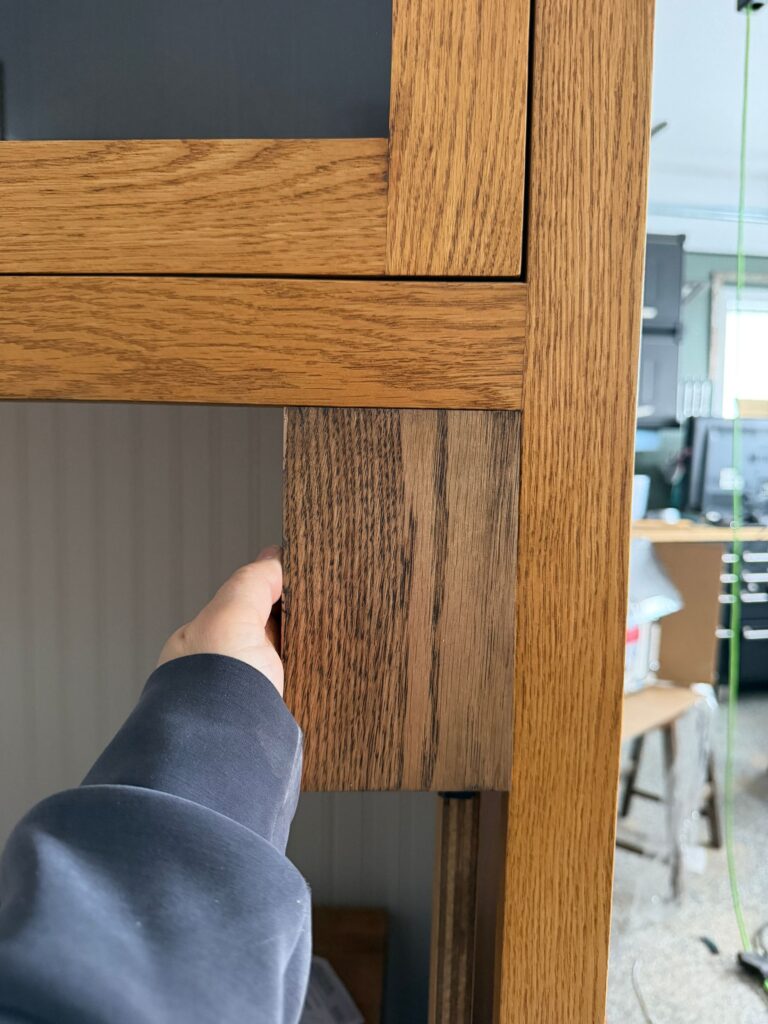 Holding a darker stain sample versus the current stain of the DIY coffee bar.