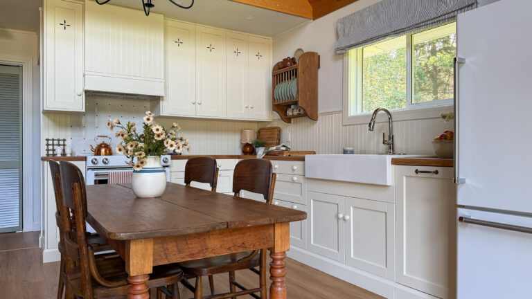 cream coloured kitchen with upper cabinet cut outs, antique farm table, farmhouse sink, wooden plate rack, and wood countertops
