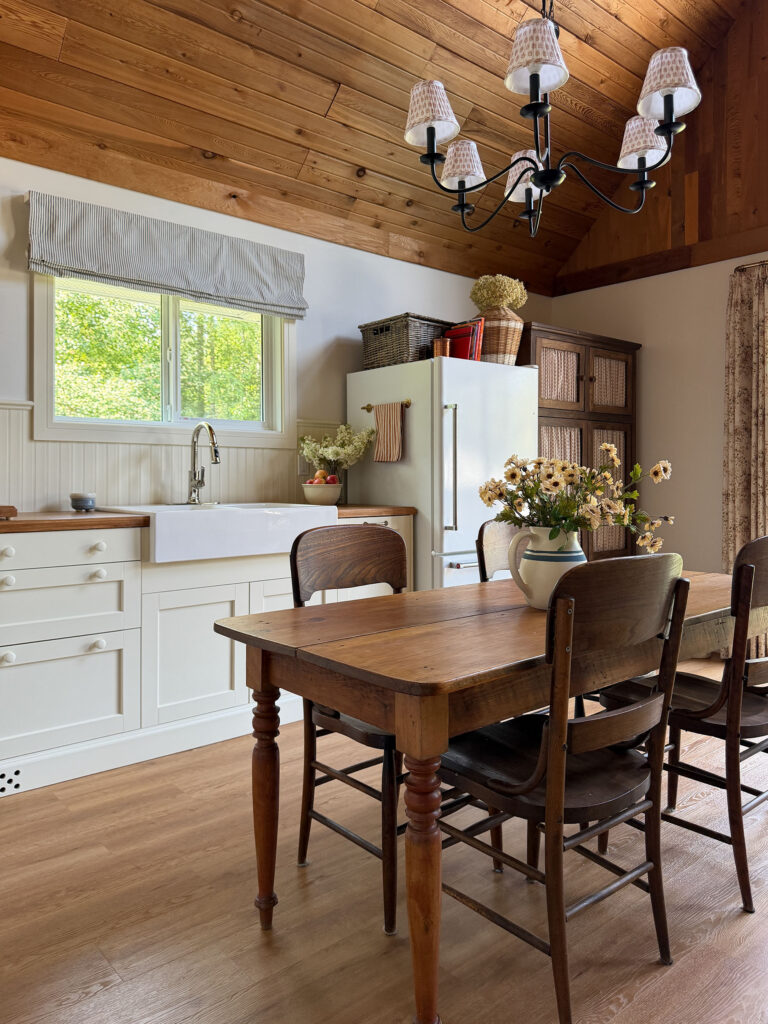 cream coloured kitchen with upper cabinet cut outs, antique farm table, farmhouse sink, wooden plate rack, and wood countertops