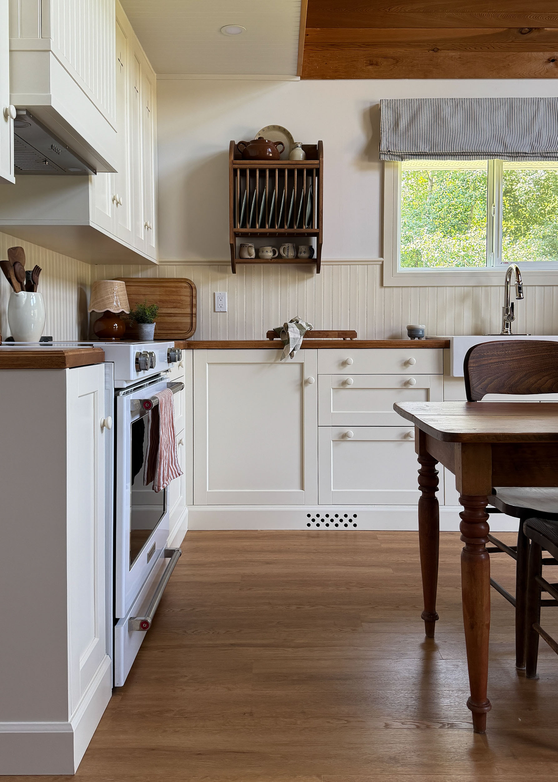 Ikea kitchen with cream coloured cabinets, butcherblock counters, antique table, freestanding wood pantry, plate rack