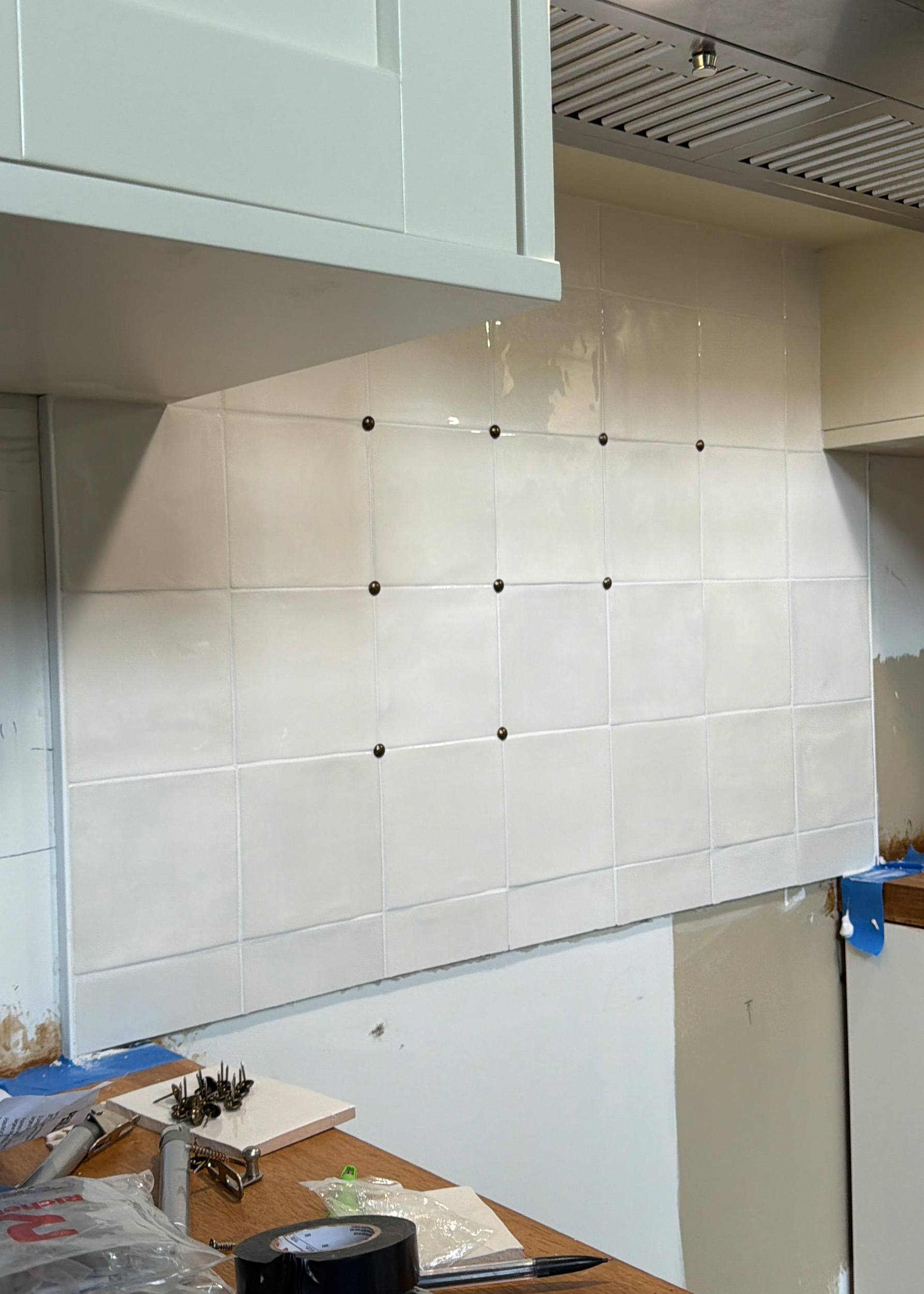 A stove with a white square tile backsplash and pins in the tile corners partially installed